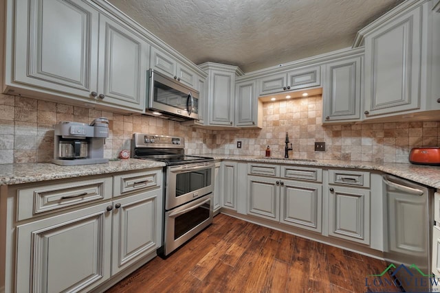 kitchen with sink, light stone counters, dark hardwood / wood-style flooring, stainless steel appliances, and decorative backsplash