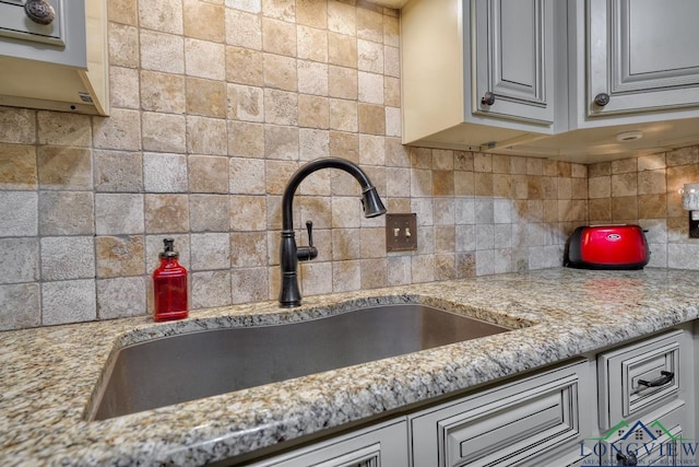 kitchen featuring light stone counters, sink, and decorative backsplash