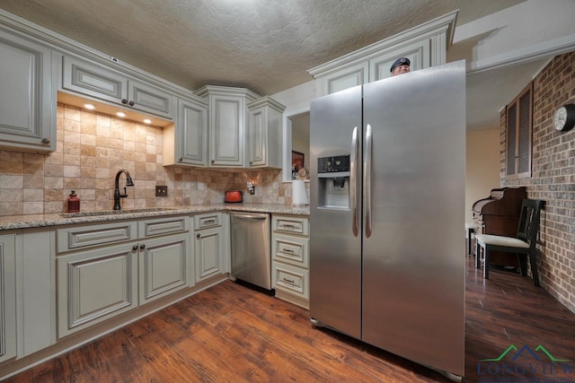 kitchen featuring dark wood-type flooring, sink, stainless steel appliances, light stone countertops, and backsplash