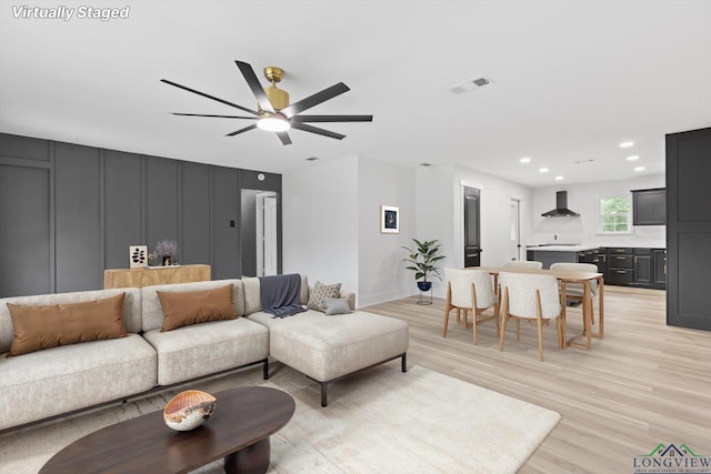 living room with a decorative wall, a ceiling fan, light wood finished floors, visible vents, and recessed lighting