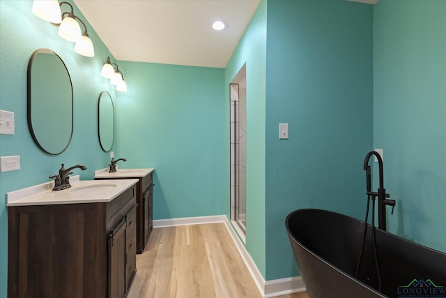bathroom with a shower stall, wood finished floors, a freestanding tub, vanity, and baseboards