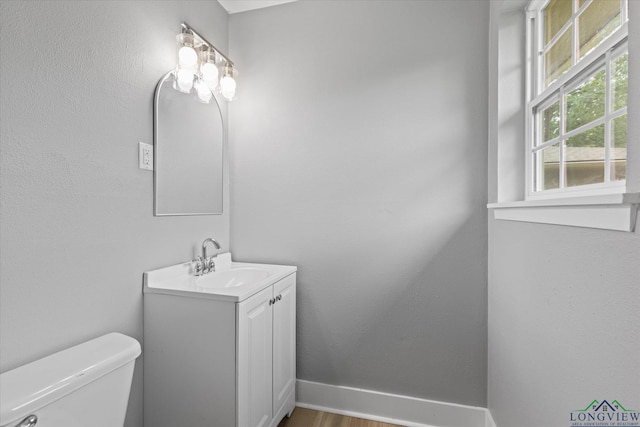 half bath with baseboards, toilet, vanity, and wood finished floors