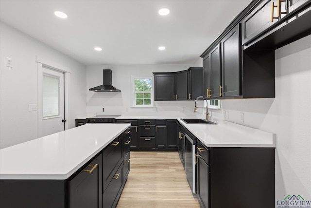 kitchen with a sink, light wood finished floors, light countertops, wall chimney exhaust hood, and recessed lighting