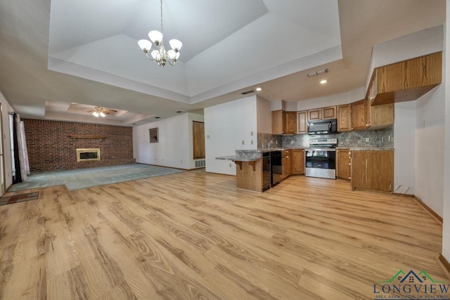 kitchen featuring a fireplace, decorative light fixtures, a kitchen breakfast bar, black appliances, and a raised ceiling