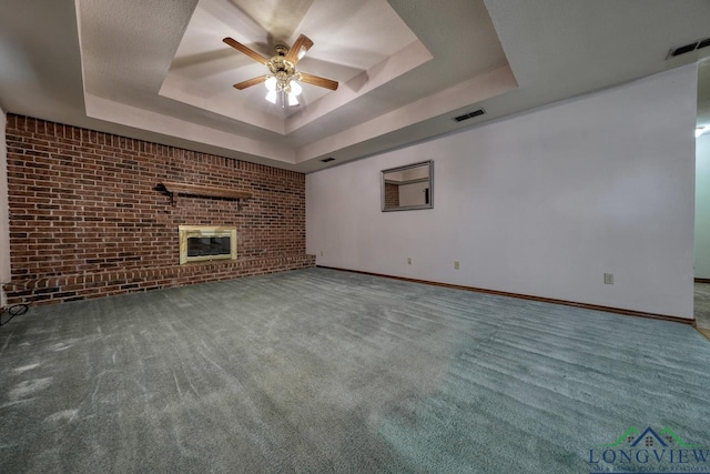 unfurnished living room with brick wall, a fireplace, carpet floors, ceiling fan, and a raised ceiling