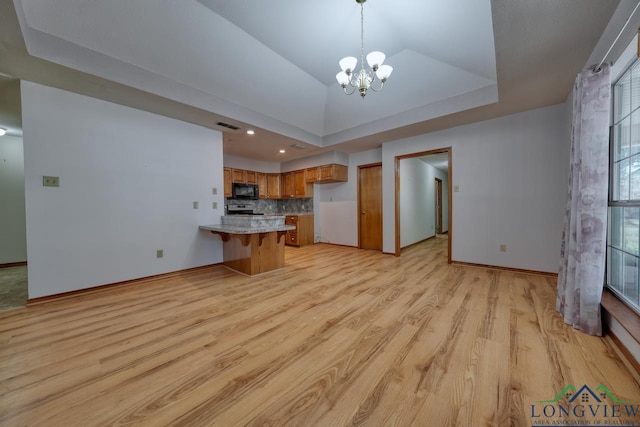 unfurnished living room with a raised ceiling, vaulted ceiling, a notable chandelier, and light wood-type flooring