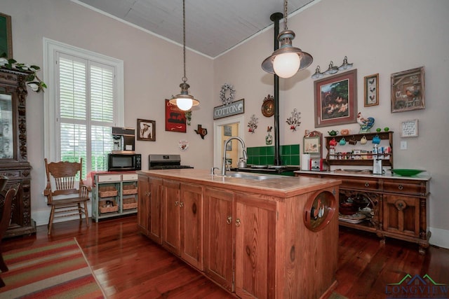 kitchen with pendant lighting, a kitchen island with sink, dark wood-type flooring, sink, and ornamental molding