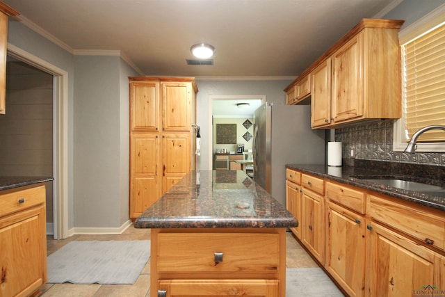 kitchen with a sink, tasteful backsplash, dark stone counters, freestanding refrigerator, and crown molding
