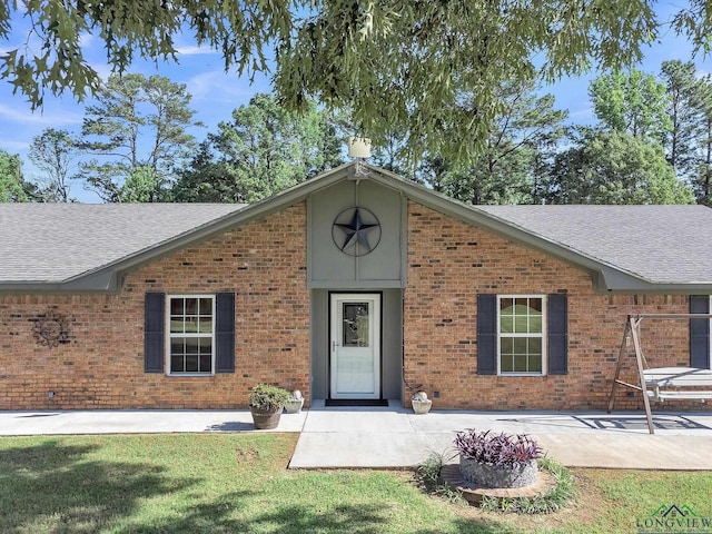 view of front of home with roof with shingles, brick siding, a front lawn, and a patio area