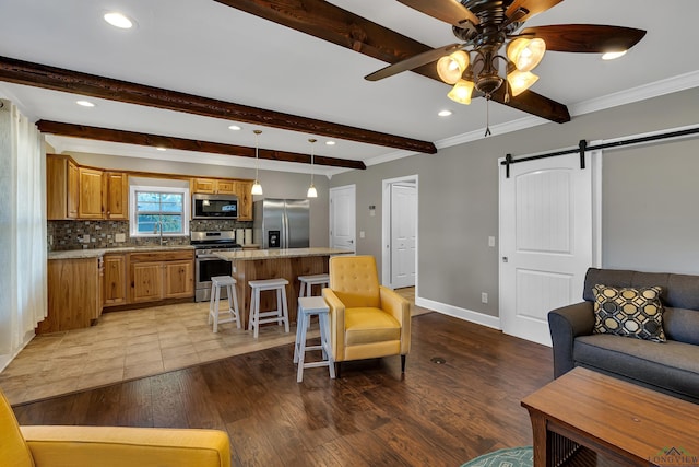 living room with ceiling fan, a barn door, sink, beamed ceiling, and light wood-type flooring