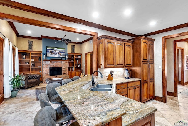 kitchen featuring ceiling fan, kitchen peninsula, sink, light stone countertops, and a breakfast bar area