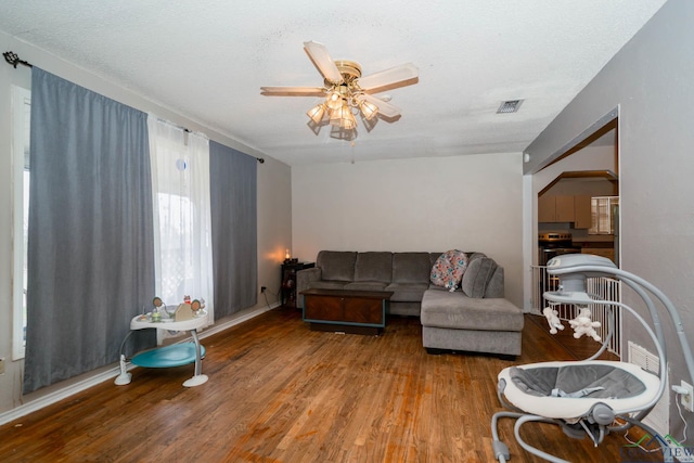 living area featuring visible vents, a textured ceiling, wood finished floors, and a ceiling fan