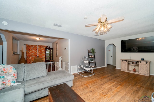 living room with a ceiling fan, wood finished floors, visible vents, and arched walkways