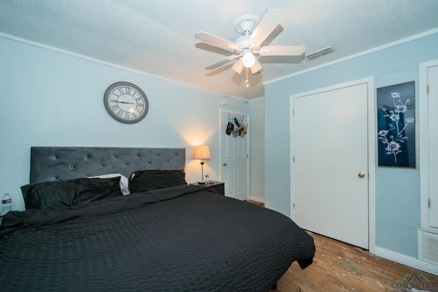 bedroom featuring ceiling fan, wood finished floors, visible vents, and ornamental molding