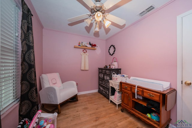 interior space featuring visible vents, baseboards, light wood-type flooring, ornamental molding, and a ceiling fan