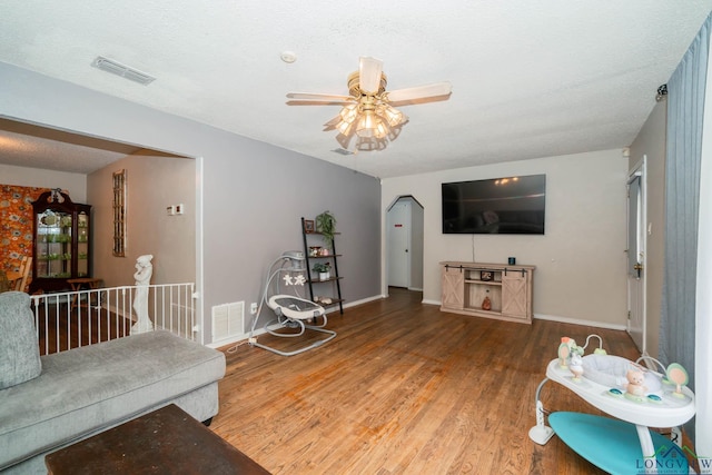 living room featuring visible vents, a textured ceiling, baseboards, and wood finished floors