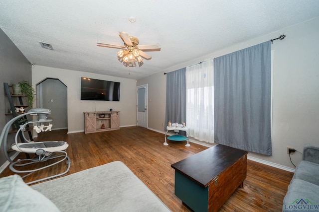 living room featuring visible vents, a ceiling fan, a textured ceiling, wood finished floors, and baseboards