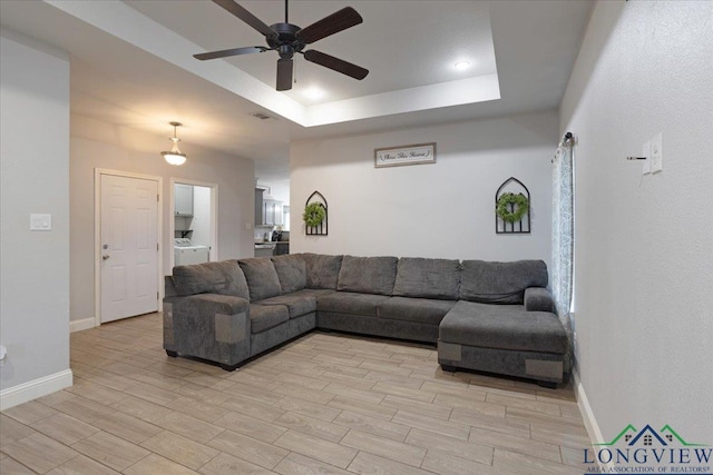 living room featuring a raised ceiling, light wood-style flooring, a ceiling fan, and baseboards