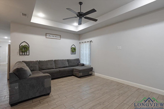 living area featuring light wood finished floors, a tray ceiling, visible vents, baseboards, and ceiling fan