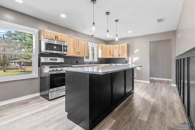 kitchen with pendant lighting, a kitchen island, light brown cabinets, stainless steel appliances, and light stone counters