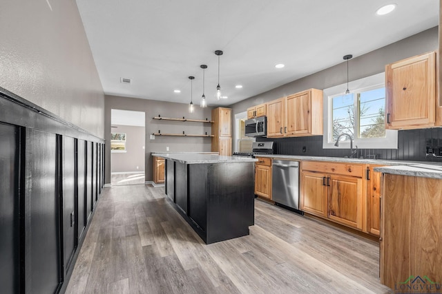 kitchen with appliances with stainless steel finishes, pendant lighting, light hardwood / wood-style floors, and a kitchen island