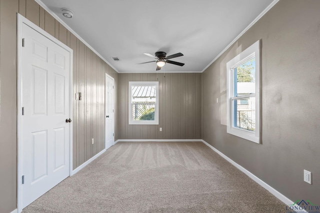 carpeted empty room featuring ceiling fan, wood walls, and crown molding