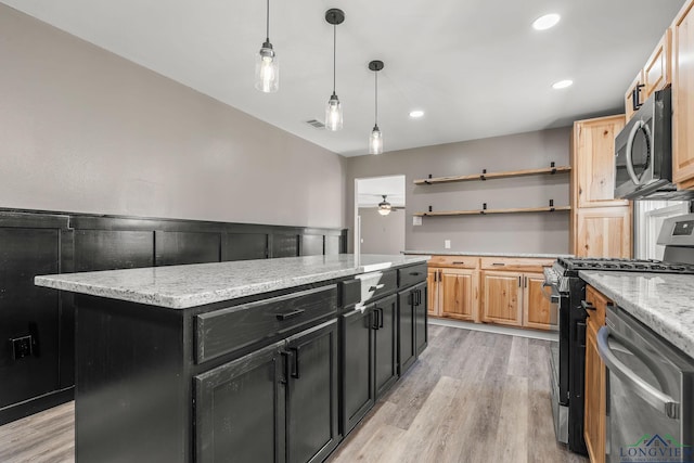 kitchen featuring ceiling fan, appliances with stainless steel finishes, light stone countertops, light hardwood / wood-style flooring, and a center island