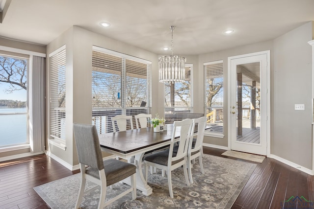 dining area with a wealth of natural light, an inviting chandelier, and dark hardwood / wood-style flooring