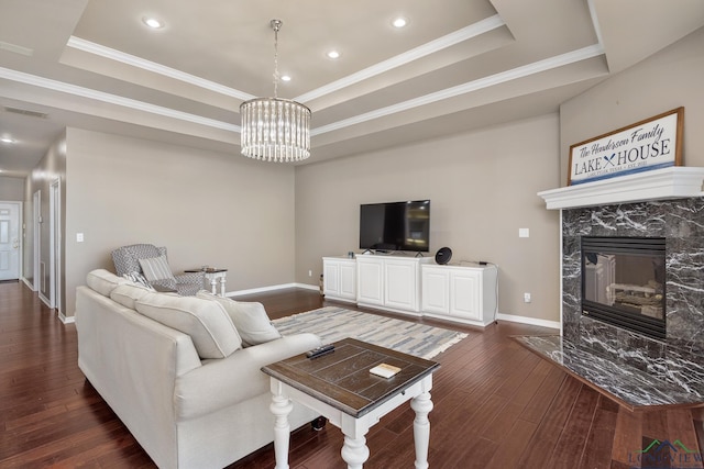 living room with crown molding, a chandelier, dark hardwood / wood-style floors, a tray ceiling, and a high end fireplace