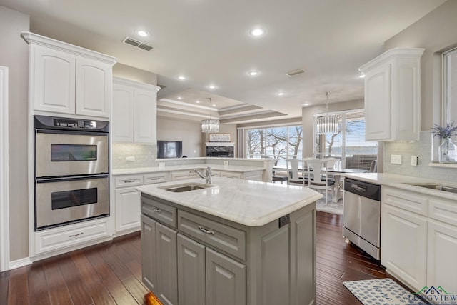 kitchen featuring sink, a center island with sink, appliances with stainless steel finishes, a tray ceiling, and white cabinets