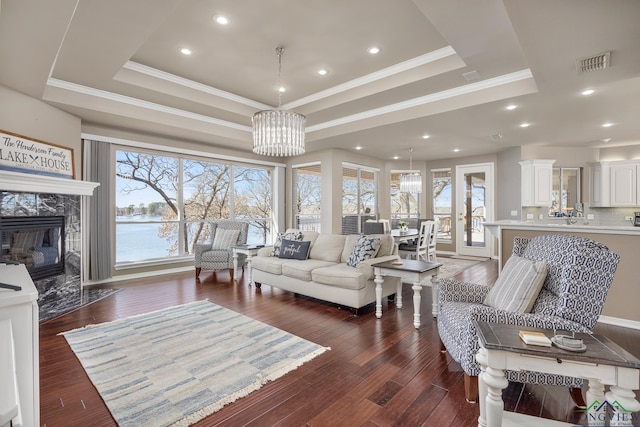 living room featuring a premium fireplace, dark wood-type flooring, an inviting chandelier, and a tray ceiling