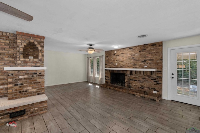 unfurnished living room with a textured ceiling, a brick fireplace, ceiling fan, and a healthy amount of sunlight