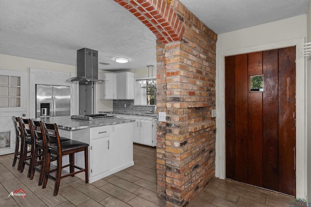 kitchen with white cabinets, range hood, a textured ceiling, and appliances with stainless steel finishes