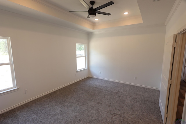 spare room with dark colored carpet, a tray ceiling, ceiling fan, and a healthy amount of sunlight