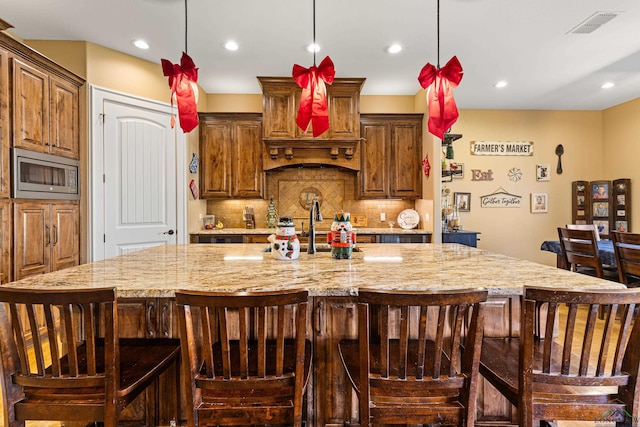 kitchen featuring tasteful backsplash, stainless steel microwave, a kitchen bar, and a large island with sink