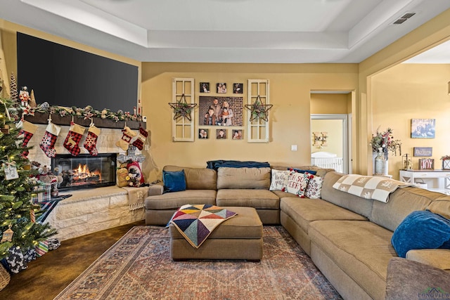 living room featuring a raised ceiling and a stone fireplace