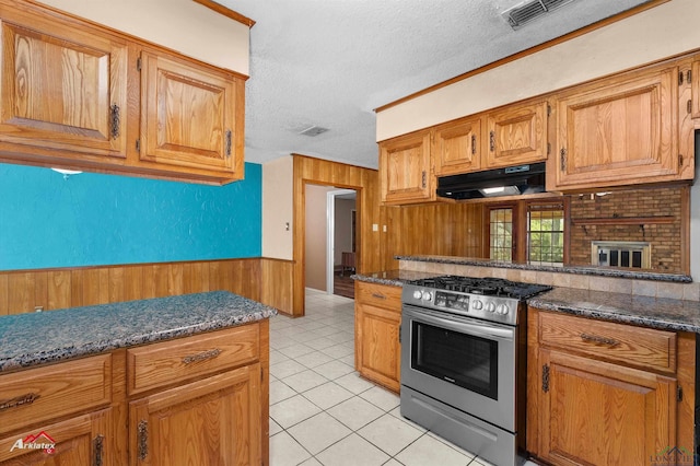 kitchen featuring stainless steel gas range, wood walls, a textured ceiling, under cabinet range hood, and visible vents