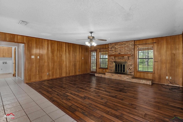 unfurnished living room featuring visible vents, wood walls, ceiling fan, and wood finished floors