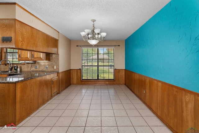 unfurnished dining area with a textured ceiling, a notable chandelier, wood walls, and wainscoting