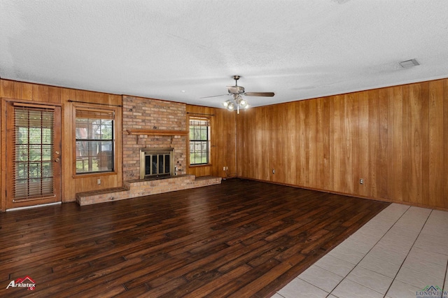 unfurnished living room featuring a ceiling fan, a fireplace, wood walls, a textured ceiling, and hardwood / wood-style floors