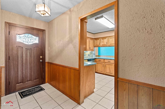 entryway with light tile patterned flooring, a textured wall, wood walls, and wainscoting