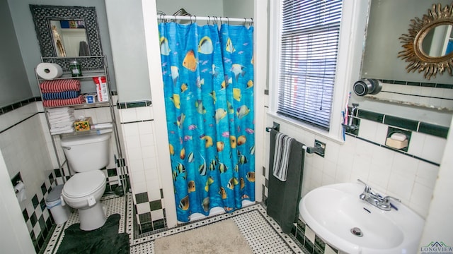 bathroom with tile patterned floors, curtained shower, sink, toilet, and tile walls