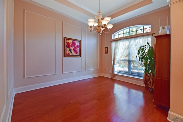 spare room with a tray ceiling, crown molding, a chandelier, and dark hardwood / wood-style floors