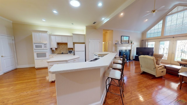 kitchen with white appliances, tasteful backsplash, a kitchen island, white cabinetry, and a breakfast bar area