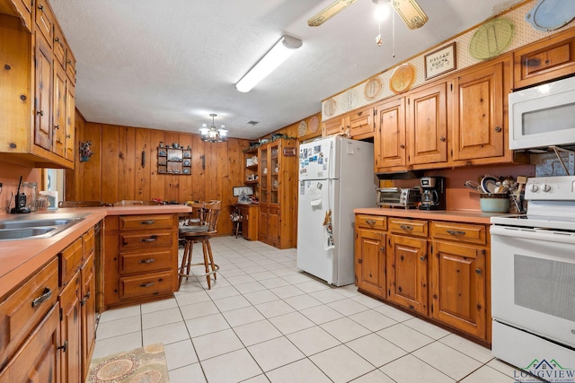 kitchen with white appliances, ceiling fan, sink, a breakfast bar area, and wood walls