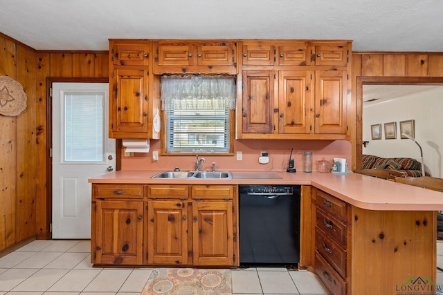 kitchen featuring sink, black dishwasher, kitchen peninsula, wood walls, and light tile patterned flooring