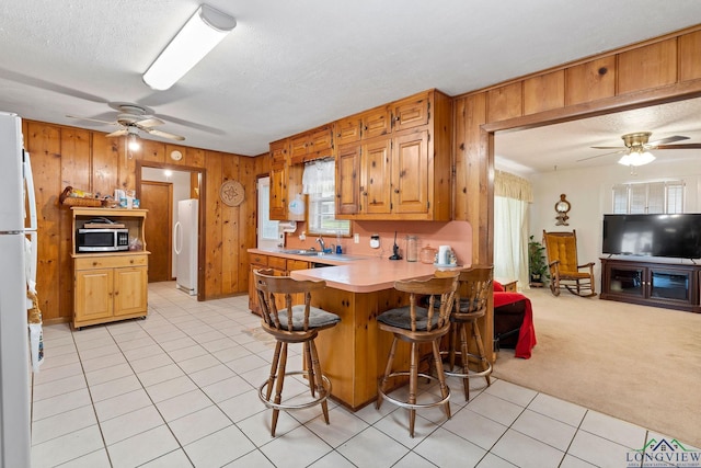 kitchen featuring a breakfast bar area, wooden walls, white fridge, and light colored carpet