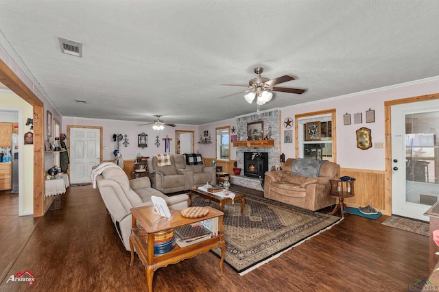 living room with crown molding, dark wood-type flooring, ceiling fan, a textured ceiling, and a stone fireplace