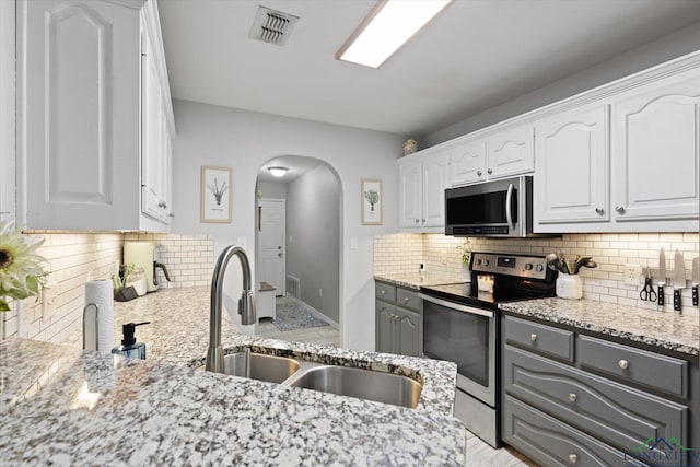 908 Victoria Dr, Longview, TX 75604 - kitchen with white cabinets, a sink, arched walkways, stainless steel appliances, and visible vents