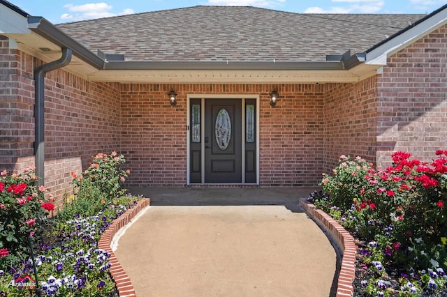 property entrance featuring brick siding and a shingled roof
